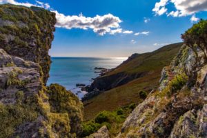 green and brown mountain beside sea under blue sky and white clouds during daytime