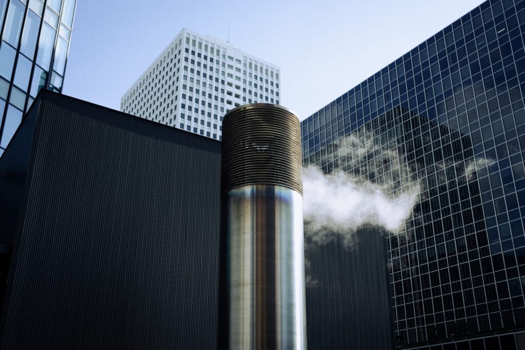 a smokestack in front of a building with skyscrapers in the background