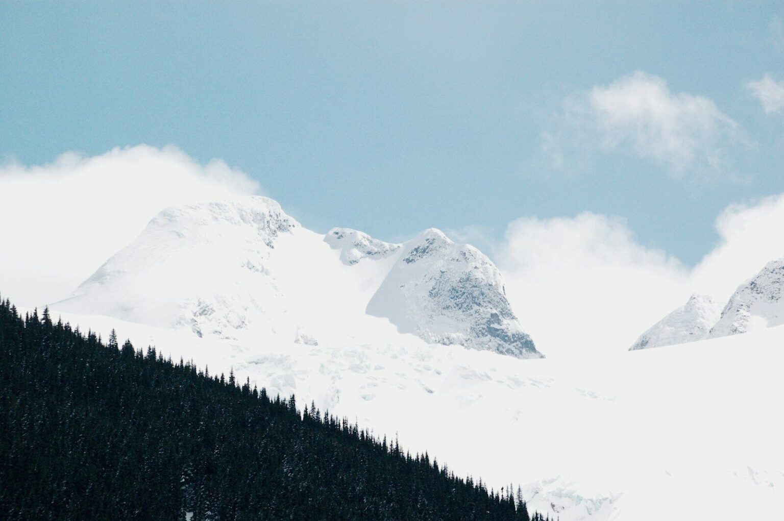 a snow covered mountain with a few clouds in the sky