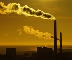 The sun is setting behind a factory with smoke coming out of it