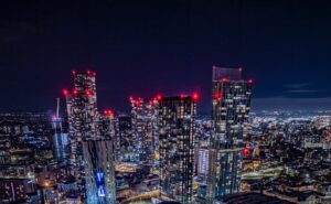 Cityscape at night with illuminated train station and skyscrapers.